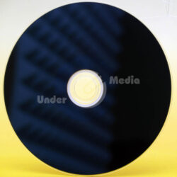 Ein blauer Blu-ray-Rohling auf einem gelben Hintergrund, mit sichtbaren Lichtreflexionen und einer zentralen Öffnung.