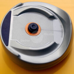 Zentrierhilfe mit einem runden Bodel und einem zentralen Kopf auf einer gelben Oberfläche.