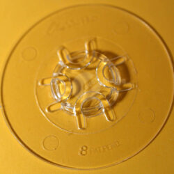 Nahaufnahme einer transparenten Form mit sechs Halterungen auf einem gelben Untergrund.