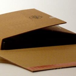 Ein halb geöffnetes braunes Paket, das einen dunklen Gegenstand zeigt, auf einer neutralen Oberfläche.