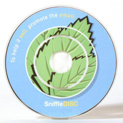 Eine kreisförmigen Disc, die für Duftwerbung entworfen wurde, mit einem Minzblatt-Design und dem Text „To help it sell, promote the smell“ auf blauem Hintergrund.