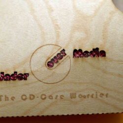 Holz-Oberfläche mit der Aufschrift "Under Over Media" und "The CD-Case Warrior" in stilvollem Design.