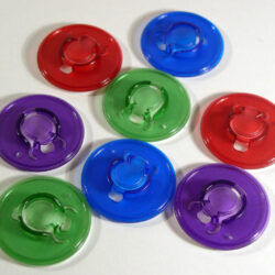 Eine Ansammlung von runden, farbigen Kunststoffdeckeln in Rot, Blau, Grün und Lila auf einem weißen Hintergrund.
