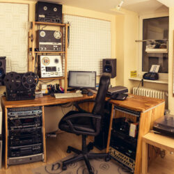 Ein Blick auf ein professionelles Aufnahmestudio mit Mischpult, Lautsprechern, analogen Bandgeräten und einem Computerarbeitsplatz.