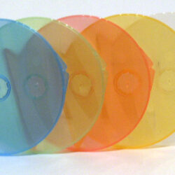 Eine Reihe von farbigen, transparenten CD-Hüllen in Fischform, angeordnet von links nach rechts in Blau, Rot, Orange, Gelb und Transparent.