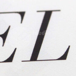 Nahaufnahme eines Buchstabens auf einer weißen Fläche, zeigt stilisierte Schriftzüge und Textur.