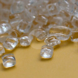 Nahaufnahme von transparenten, glasklaren Kristallen, die auf einem gelben Stoff liegen.