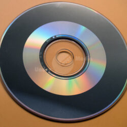 Eine digitale Compact Disc auf einem orangefarbenen Hintergrund, sichtbar mit bunten holographischen Reflexionen.