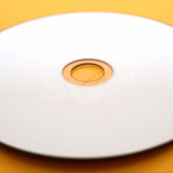 Nahaufnahme einer leeren CD mit einem transparenten Loch in der Mitte auf einem orangefarbenen Untergrund.