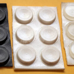 Drei Platten mit kleinen runden Aufklebern in Schwarz, Weiß und Transparent auf einem orangefarbenen Hintergrund.