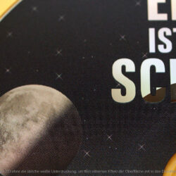 Detailansicht einer CD mit mondähnlichem Design und glänzender Schrift auf schwarzem Hintergrund