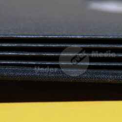 Nahaufnahme von gestapelten schwarzen Blättern in einem Ordner, auf einem gelben Untergrund.