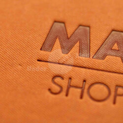 Nahaufnahme einer Prägung auf einer orangefarbenen Shoppingkarte mit dem Text "MAL" und "SHOPPING".