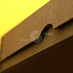 Nahaufnahme der Kante eines schwarzen Kartonbehälters vor gelbem Hintergrund.