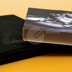 Zwei aufeinanderliegende Albumhüllen, eine schwarze und eine mit grafischem Druck, vor einem gelben Hintergrund.