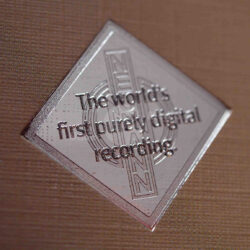 Nahaufnahme eines silbernen Emblems, das die weltweit erste rein digitale Aufnahme beschreibt.