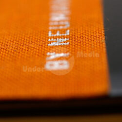 Detailaufnahme eines orangefarbenen Stoffes mit sichtbarer Naht und schwarzem Hintergrund.