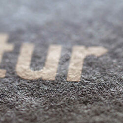 Nahaufnahme eines grau strukturierten Materials mit dem Wort „Natur“ in heller Schrift.