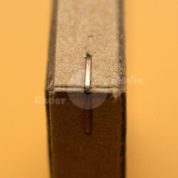 Nahaufnahme einer Heftklammer auf der Kante eines Kartons vor orangefarbigem Hintergrund