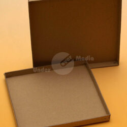 Zwei quadratische, braune Kartonrahmen, einer oben stehend und der andere in liegender Position auf einer gelben Oberfläche.