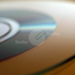 Detailaufnahme einer teilbesputterten, reflektierenden Compact Disc auf gelbem Hintergrund