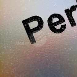 Nahaufnahme des Wortes 'Perfekte' auf einer reflektierenden Oberfläche, hinterlegt mit orangem Stoff.