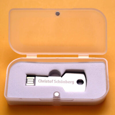 Ein eleganter USB-Stick in Schlüsselform mit dem Namen "Christof Schönberg" in einer transparenten Box aus Schaumstoff.