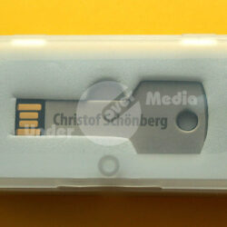 Ein USB-Speicher in Form eines Schlüssels, präsentiert in einer transparenten Aufbewahrungsbox auf gelbem Hintergrund.