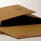 Ein halb geöffnetes braunes Paket, das einen dunklen Gegenstand zeigt, auf einer neutralen Oberfläche.