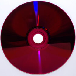 Ein dunkelroter CD-Rohling mit glänzender und spiralförmiger Oberflächenstruktur, auf weißem Hintergrund.